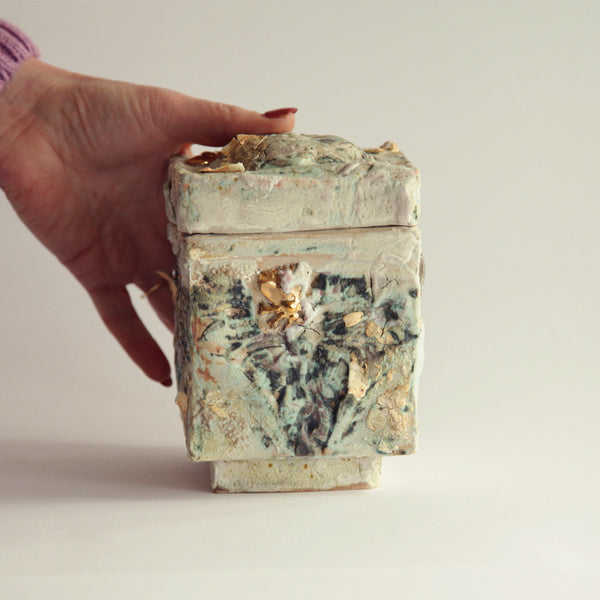Hand holding a decorative stone box with floral patterns on a plain background